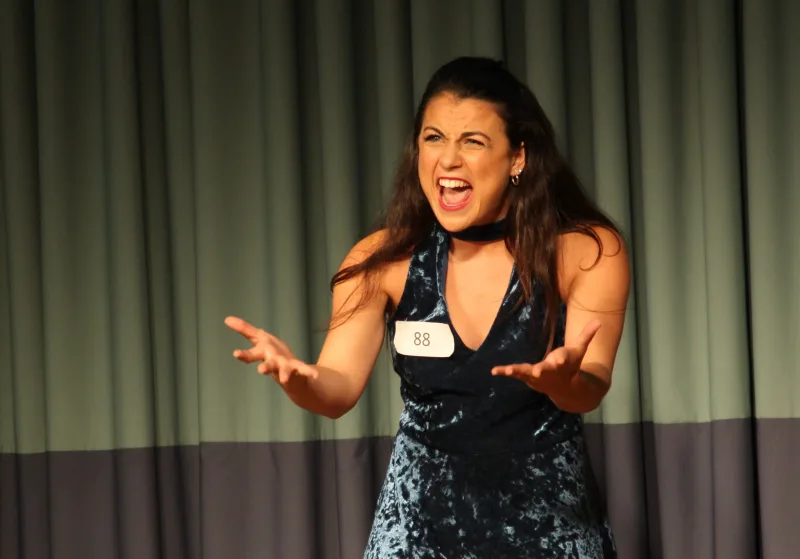 An actor singing with both hands open and stretched toward the audience