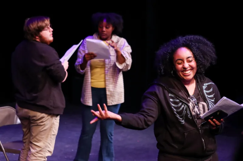 Three actors onstage with scripts in their hands