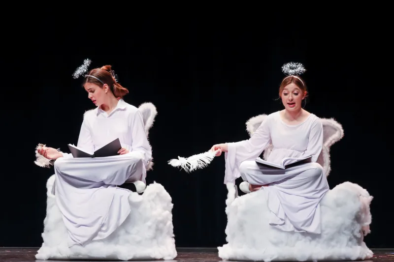 Two actors, costumed like angels, sitting in fluffy chairs with scripts in their laps